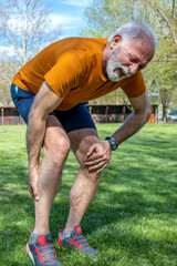 Senior athlete man frowning with muscle pain during training outdoors. Calf leg cramps trauma. Vertical orientation. - obrazy, fototapety, plakaty