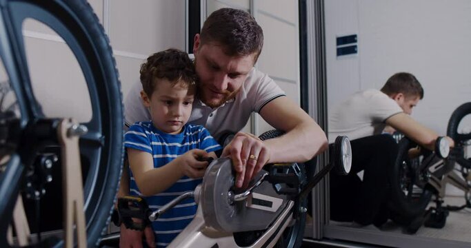 The young father helps his son repair the bicycle with tools in the house.