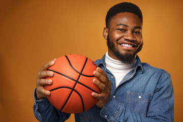 African american man holding basketball ball and looking at camera on yellow background