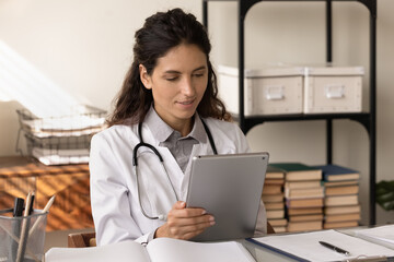Tablet in doc job. Young latin woman in white coat medical lab worker use pad study resent clinical...