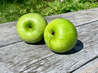 Two green apples on a gray wooden table. Close-up.