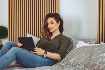 Relaxing at home. Beautiful young woman using tablet while lying on the bed.