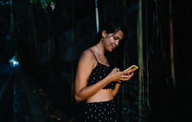 Smiling ethnic woman messaging via smartphone on street