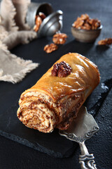 Roll with walnuts and honey. Fresh baked goods. Vertical photo.Black background.Vintage dessert spatula. Walnuts are out of focus.