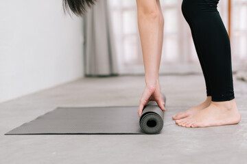 Hands of an attractive young woman folding black yoga or fitness mat after working out at home in living room or in yoga studio. Close up view photo