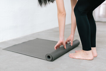 Hands of an attractive young woman folding black yoga or fitness mat after working out at home in living room or in yoga studio. Close up view photo