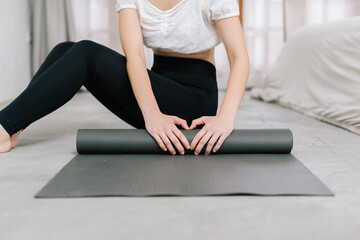 Hands of an attractive young woman folding black yoga or fitness mat after working out at home in living room or in yoga studio. Close up view photo