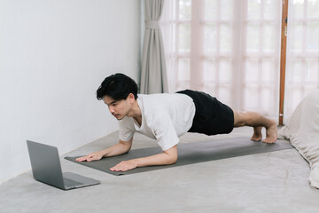 Training At Home. Sporty man doing yoga while watching online tutorial on laptop, exercising in living room, free space