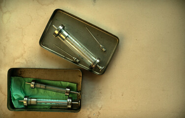 Glass medical syringes with needles in metal containers on the table.