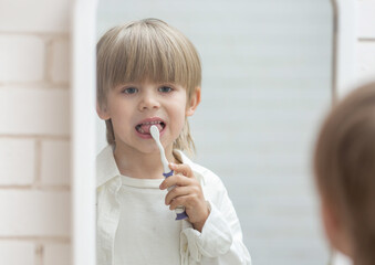 the boy is standing in front of the mirror with a toothbrush, brushing his teeth and making a funny face. He doesn't like toothpaste