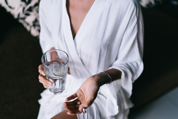 Unrecognizable ethnic woman taking pills with glass of water