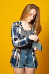 Teen girl holding wallet with dollar banknotes on yellow background. Money savings concept