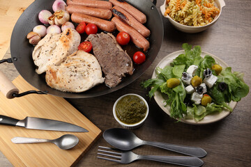 Mix meet chicken beef steak sausage tomato onion garlic fry grill oil metal fry pan colourful pasta green salad with cheese olive mint basil pesto sauce board knife fork spoon rustic wooden table