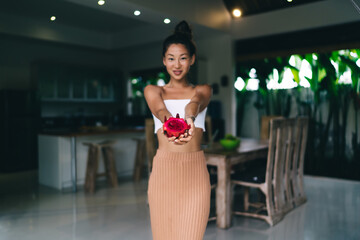 Content Asian woman demonstrating ripe fresh dragon fruit in apartment