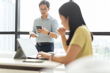 Businessman using smart phone paying bills with woman working on laptop.