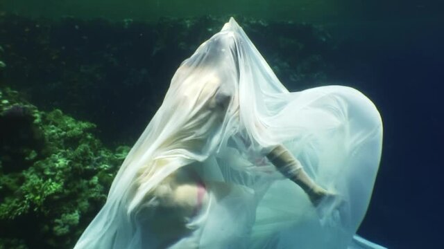 Young woman underwater model in white cloth on background of blue water. Concept of creativity and art of creating images.