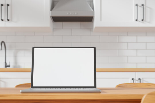 Modern laptop with white blank mockup screen on the dining table at cozy kitchen.