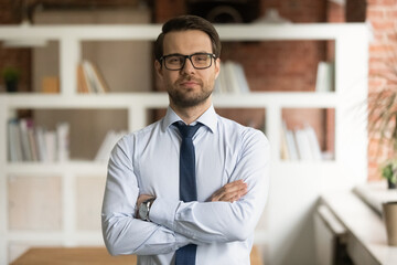 Head shot portrait confident businessman in glasses standing in office with arms crossed, successful