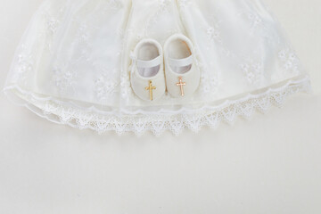 Christening background with baptism baby dress, shoes, and cross on pastel background