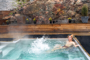 Man bathes or takes bath in small pool with hot water. Hot springs for bathing and wellness are specially equipped. Healthy mid aged male relaxing with outdoor spa treatments. SPA hotel lifestyle.