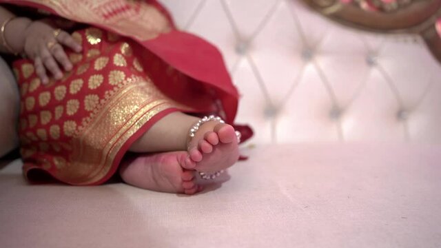 A closeup of an Indian baby wearing Banarasi with jewellery and sitting on a sofa shot in HD
