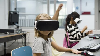 Children enjoying process of using VR glasses. Blonde girl looking around surprisingly. Boy sitting behind imagining that he struggling with somebody. VR technology in education concept. - Powered by Adobe