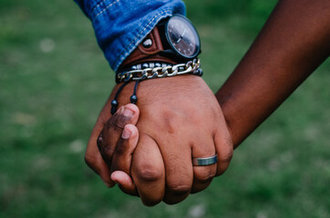 father holding the hand of his son both of brown skin, with bracelets and watch - obrazy, fototapety, plakaty