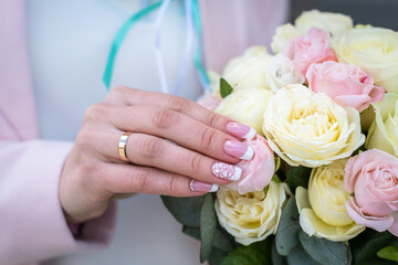 Bride holding bridal bouquet of roses. Wedding ring on finger.