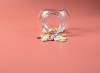 Colored pills scattered from a glass jar, against a bright pink background. The concept of medicine and treatment for coronavirus. Copy space. Selective focus.