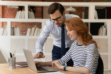 Confident mentor coach businessman in glasses training smiling new employee intern, pointing at...