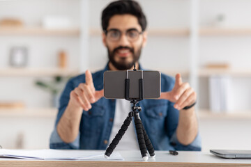 Modern hobby and remote work online. Focus on smartphone on tripod and smiling guy with glasses...