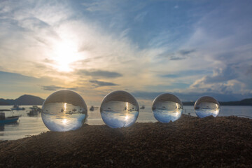.The 4 glass balls are arranged from large to small placed on the beach at sunrise. .To see the sea upside down in a glass ball. A image for a unique and creative travel idea...