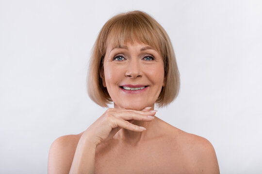 Attractive senior lady with bare shoulders showing smooth skin after cosmetic anti-aging procedure over light background