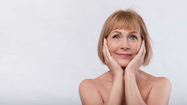 Lovely senior woman with soft skin looking at camera, touching face on light background, banner design with copy space