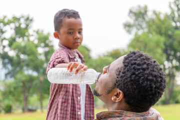 Son giving water to his father, African American dad, and son at outdoor, Happiness family in park concepts
