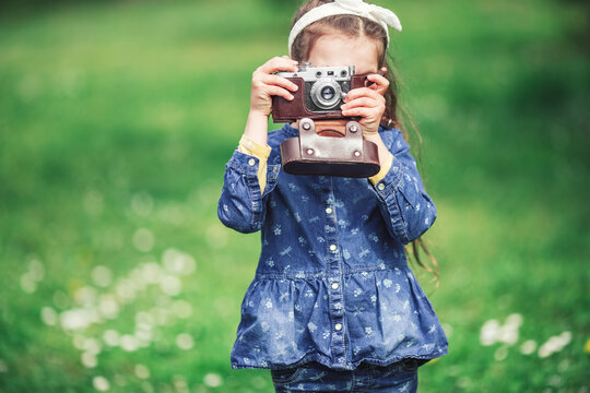 Little girl with old vintage camera making photos of surrounding nature in the park