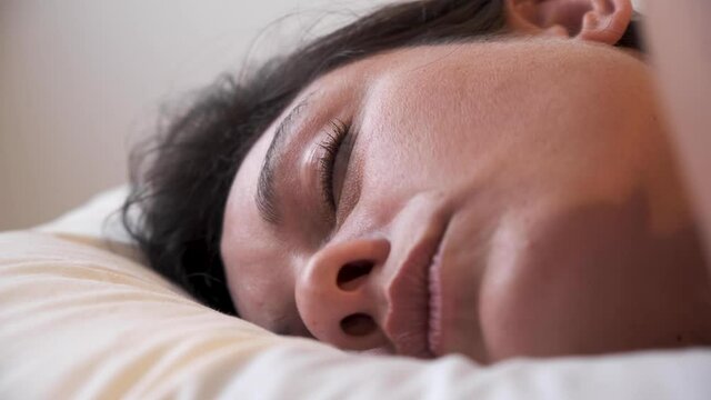 Woman sleeping in bed head on pillow CLOSE UP. Young beautiful lady laying relaxed with her eyes opened and then closed. siesta time sensual sexy girl taking a nap. noon summertime white beddings. 