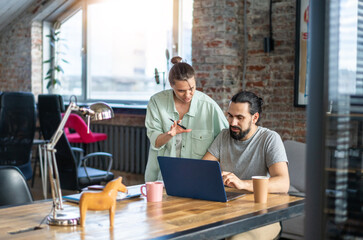 Young people hipster man and woman working in office on project using laptop while sitting at table