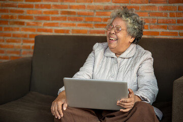 Smiling senior woman wave to camera having video call on laptop, happy elderly female sitting on sofa at home talk using modern technologies and wireless connection.