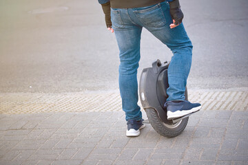 Electric unicycle, man in jeans and sneakers commuting to work on monowheel. Portable individual transportation vehicle. Man moves around city on his own electric device. Individual mobility. © Tricky Shark