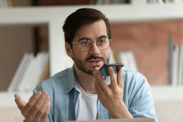 Close up confident businessman in glasses recording voice audio message on smartphone, serious man...