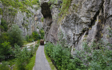 Aerial drone view of a truck transporting timber on a road that winds along the vertical stone walls of a sharp, steep canyon located in Sohodol Gorges. Carpathia, Romania.