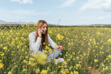 Fototapeta premium Young woman talking to the telephone in a field of yellow flowers