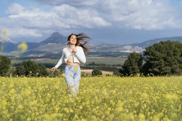 Young woman running happy in a field of yellow flowers