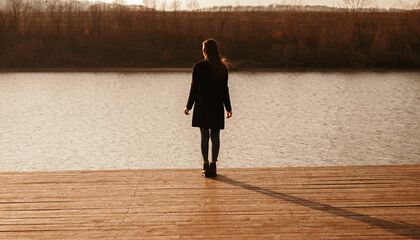 Woman in black outfit standing on pier near river