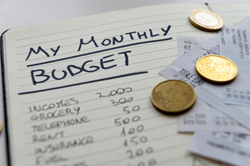 Page of notepads with monthly expense budgets, with receipts and invoices beside them, and coins. Monthly budget.
