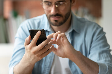 Close up cropped of confident businessman in glasses using smartphone, typing and looking at...