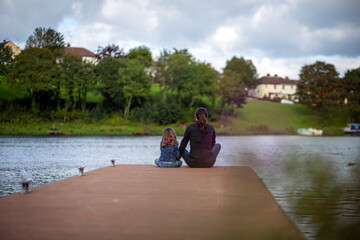 Fototapeta na wymiar Mother and daughter with their backs turned and sitting on a jetty enjoying the views of the river in UK.