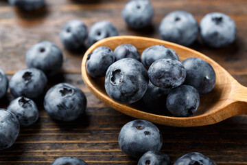Fresh blueberries in a wooden spoon. The berries are scattered on a wooden table. Vegan and vegetarian concept.