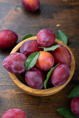 Fresh plums with leaves in a wooden bowl on a brown table.